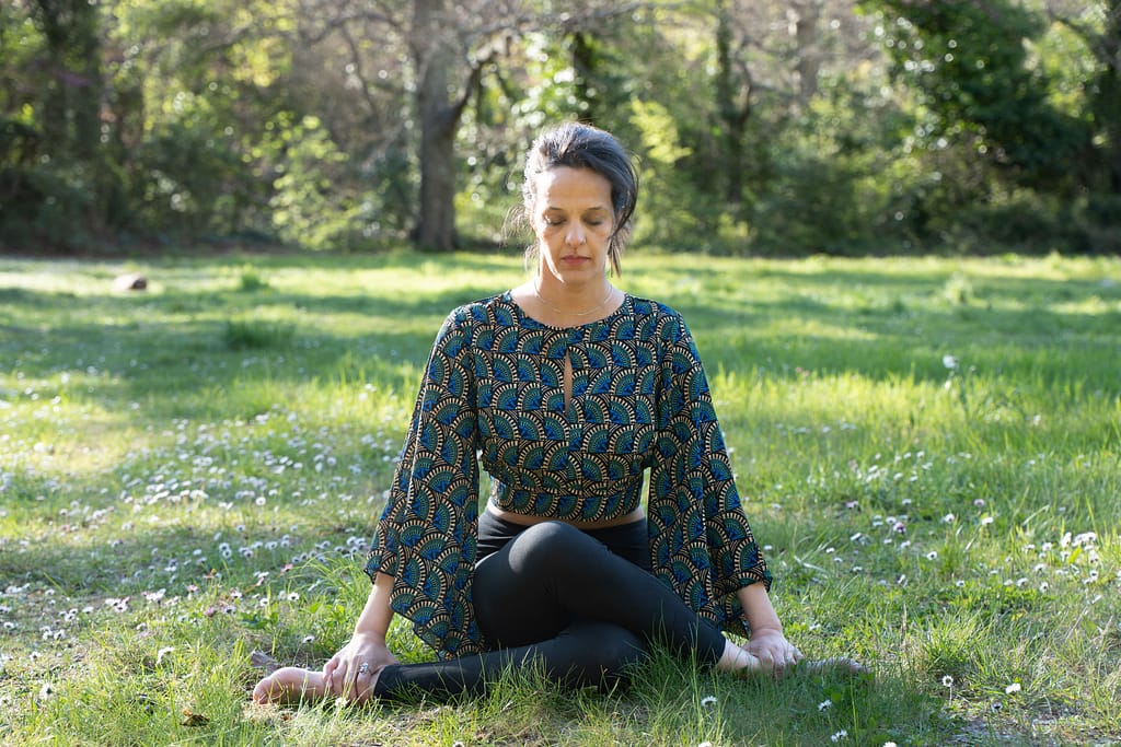 Femme assise en méditation dans l'herbe, retour au calme du système nerveux